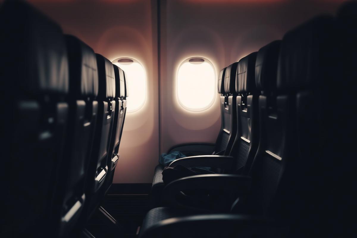 Rows of economy aeroplane seats lit by cabin windows, one seat reclined